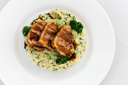 Grilled chicken slices rest atop a creamy spinach mashed potato base garnished with fresh broccoli.の写真素材