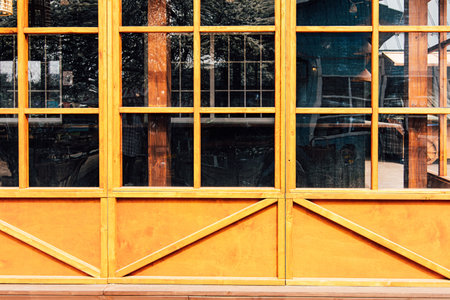Sunlight reflects off the vibrant yellow wooden frames of a buildings windows highlighting their rustic charm in a lively outdoor setting.の写真素材