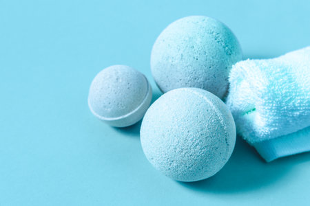 Several bath bombs of varying sizes rest on a soft blue surface next to a white towel creating a soothing atmosphere for relaxation.の写真素材