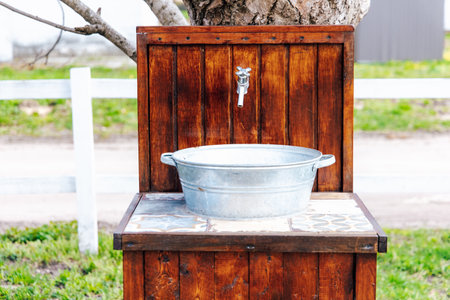 An outdoor wash basin made of metal and wood placed under a tree in a green garden perfect for cleaning or rinsing.の写真素材