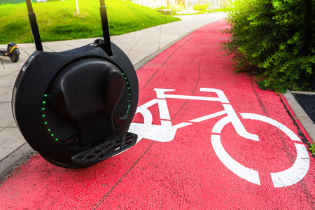 A sleek unicycle rests near a painted bicycle symbol on a vibrant red bike lane in a sunny urban...