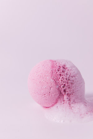 A vibrant pink bath bomb is dissolving creating a frothy bubble effect on a soft pink background. Perfect for a soothing bath experience.の写真素材