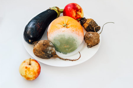 Fresh vegetables and fruits including eggplant, apples, and a melon are arranged on a white plate...