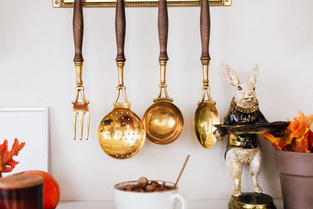 Brass utensils hang from a wall alongside an elegant rabbit figure creating a warm and inviting kitchen atmosphere filled with homey decor.の写真素材