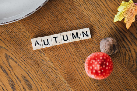 Wooden letters spell autumn surrounded by a colorful leaf and acorn on a rustic wooden table showcasing seasonal decor.の写真素材