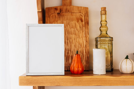 A wooden shelf showcases a blend of autumn decorations with various pumpkins and an empty frame for seasonal display.の写真素材