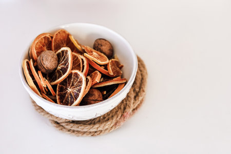 Colorful dried citrus slices and whole nuts fill a bowl on a natural rope mat creating a charming display for decor.の写真素材