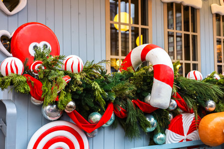 Colorful holiday decorations adorn a storefront featuring red and white candy canes baubles and...