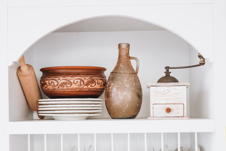 A shelf showcases a variety of rustic kitchen items including a clay pot an old pitcher a wooden rolling pin and plates arranged neatly.の写真素材