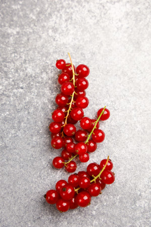 Vibrant red currants lay neatly on a gray stone surface showcasing their fresh appeal for desserts...