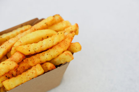Golden fried potatoes seasoned with spices fill a brown box ready for enjoyment at a casual dining location.の写真素材