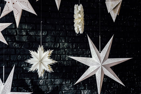 White paper stars of various shapes are beautifully displayed against a black brick wall creating an...