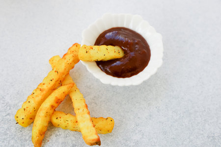 Golden crispy fries are dipped into a rich brown sauce on a neutral gray background perfect for a...