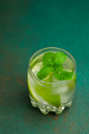 A mojito cocktail is presented in a clear glass filled with ice fresh mint leaves and lime slices.