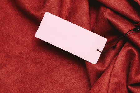 A simple blank tag lies on rich red fabric highlighting the softness and texture of the material...