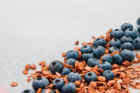 Fresh blueberries and crunchy granola are artistically arranged on a smooth gray surface highlighting a healthy snack choice.の写真素材