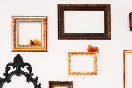 A collection of ornate empty frames is displayed on a bright wall featuring colorful autumn leaves...