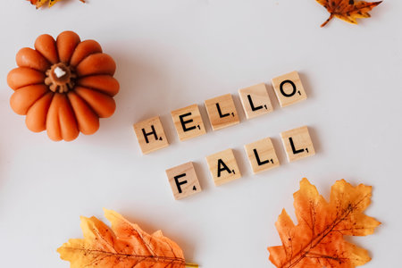 Decorative wooden letters spell out a warm greeting for autumn amidst colorful leaves and a small pumpkin. The festive arrangement captures the essence of fall inviting seasonal cheer.の写真素材