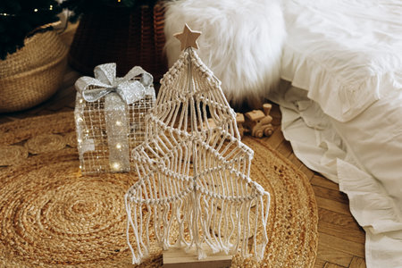 A decorative macrame Christmas tree stands on a warm woven rug in a cozy living room. Next to it a...