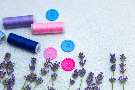 Bright spools of thread in purple blue and pink lay beside colorful buttons. Fresh lavender stems...