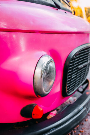This close view captures a bright pink vintage car with its distinctive rounded headlight and...