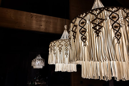 Three detailed macrame chandeliers hang gracefully in a dimly lit room casting a warm glow and...