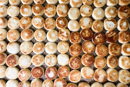 Golden syrniki cheesecakes rolls are placed in neat rows on a tray. The warm soft texture and...