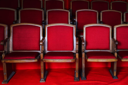 Vintage red chairs are lined up in rows within an empty auditorium. The polished wooden frames...