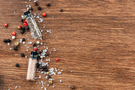 Various spices and salts are scattered across a wooden table showcasing different textures and...
