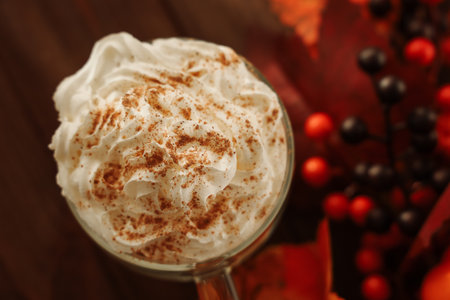 A close view of a glass filled with whipped cream topped with cinnamon surrounded by autumn leaves and vibrant berries. The cozy atmosphere evokes a sense of warmth and seasonal comfort.の写真素材