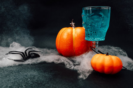 A festive Halloween display features vibrant orange pumpkins alongside a skull shaped glass filled with a blue drink.の写真素材