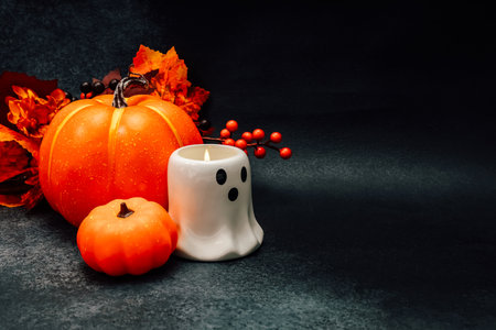 A vibrant orange pumpkin and a small pumpkin sit beside a ghost shaped candle. Bright red berries and autumn leaves enhance the spooky atmosphere perfect for Halloween decorations.の写真素材
