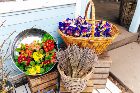 Brightly colored flowers are placed in woven baskets outside a charming shop. The scene showcases a mix of fresh blooms and dried lavender creating a lively spring atmosphere.の写真素材