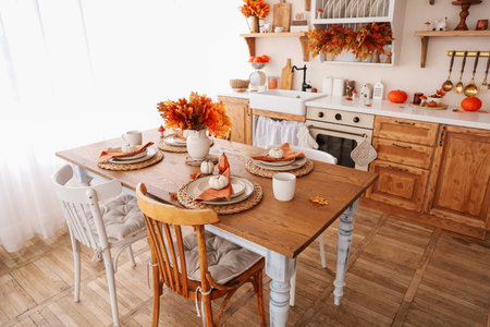 This inviting dining space features a rustic wooden table set with autumn decorations. Colorful leaves white pumpkins and warm tones create a cozy atmosphere perfect for family gatherings in fall.の写真素材