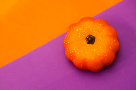 A vibrant orange pumpkin sits on a bright purple and orange background adding a cheerful touch to autumn decorations. The pumpkin features a textured surface.の写真素材