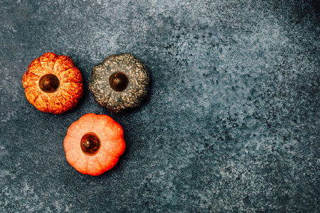 Three decorative pumpkins in vibrant colors are arranged on a textured dark surface. These pumpkins are perfect for autumn celebrations evoking seasonal warmth and festive spirit.の写真素材