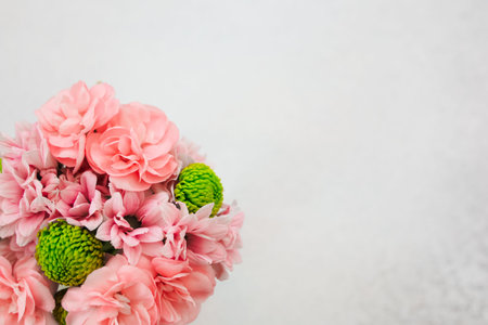 A bouquet of soft pink flowers featuring round green accents is showcased against a plain white...