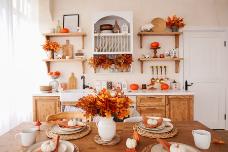 A warm kitchen showcases a table beautifully arranged for fall. There are decorative pumpkins colorful leaves and soft lighting creating an inviting atmosphere.の写真素材