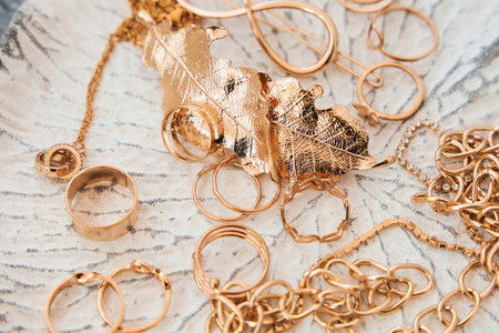 A collection of gold jewelry is arranged neatly on a textured plate. Rings chains and delicate leaves create an elegant display showcasing intricate designs and craftsmanship.の写真素材