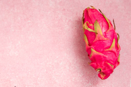 A bright pink dragon fruit rests on a soft pastel pink surface. The unique shape and color of the fruit highlight its exotic appeal. This scene promotes healthy eating and fresh produce ideas.の写真素材