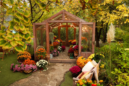 A charming greenhouse surrounded by colorful flowers is seen during the autumn season. Warm lights illuminate the space creating a cozy atmosphere. Natures beauty is fully displayed in this garden.の写真素材
