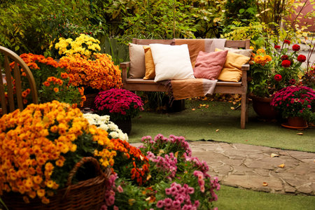 A lovely garden features a wooden bench adorned with cushions in warm tones. Surrounding the bench are clusters of blooming flowers in various colors.