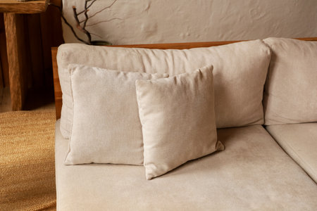 Soft beige pillows rest on a comfortable light colored couch in a warm and inviting living room. The cozy atmosphere is enhanced by natural wooden elements and a textured rug nearby.の写真素材