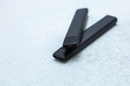 Two black electronic cigarettes on a gray background. Modern vaping devices, sleek minimalist design, nicotine alternatives, concept of smoking, technology and lifestyleの写真素材