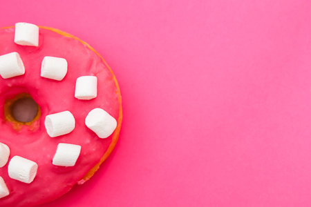 A bright pink donut sits on a vibrant pink surface adorned with fluffy white marshmallows. It looks tempting and sweet making it an appealing treat for dessert lovers.の写真素材