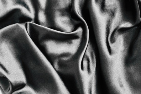 The black satin fabric lies in gentle folds showcasing its smooth texture and sheen. Soft light reflects off the surface highlighting the elegant drapes and creating a rich luxurious appearance.の写真素材