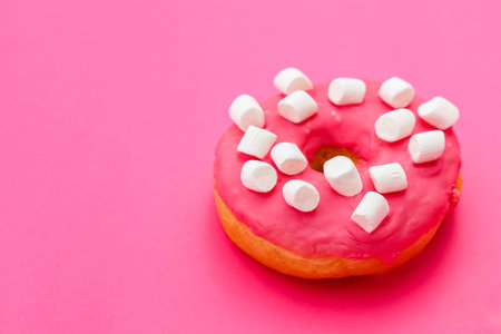 A pink frosted donut topped with small marshmallows sits on a vibrant pink background. The colorful dessert invites sweet indulgence and playful enjoyment at any time of day.の写真素材