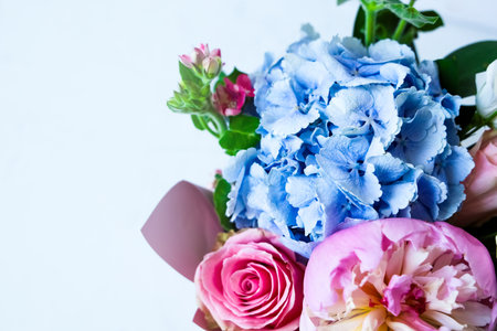 A vibrant display of flowers features soft pink roses and delicate blue hydrangeas. The arrangement sits against a light backdrop showcasing natural beauty and freshness in full bloom.の写真素材