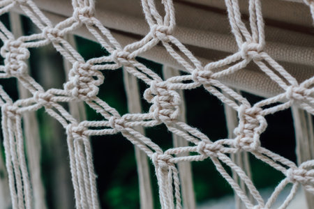 Close up view of a handwoven hammock showing intricate knot patterns made of durable rope. The background features lush greenery highlighting the serene atmosphere of outdoor relaxation.の写真素材