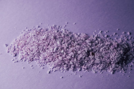 Purple rock salt is artfully spread over a simple surface showcasing its unique texture and vibrant color. The light reflects off the crystals creating a visually appealing scene of natural beauty.の写真素材